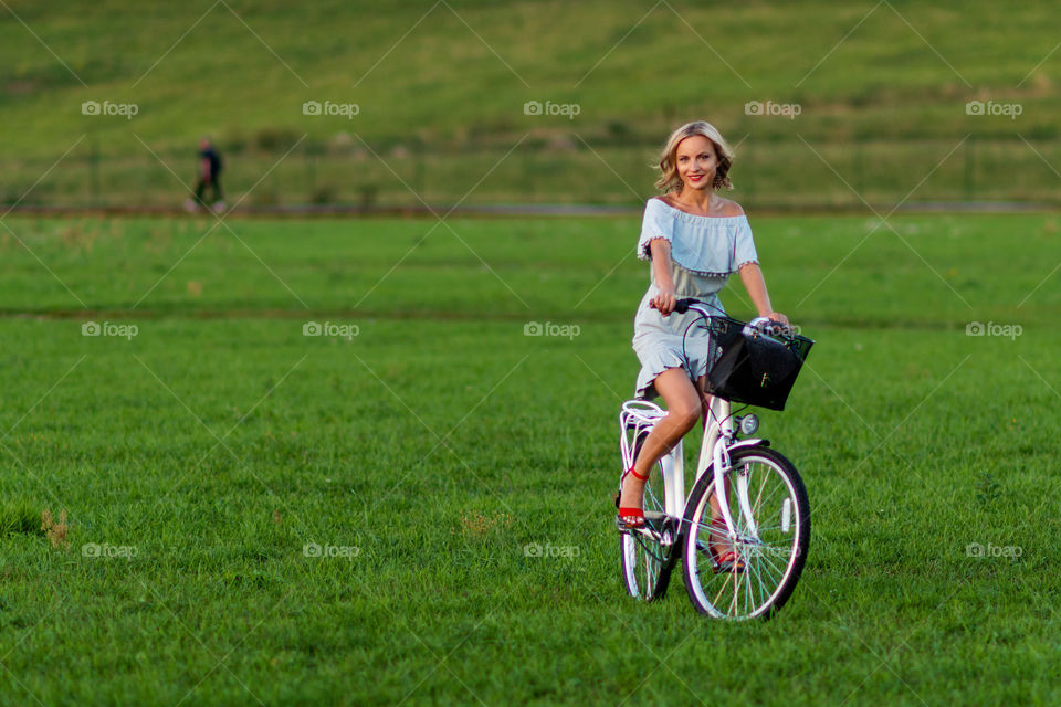 Soft focus photo. A young, beautiful blond woman with a white bike in a green meadow.