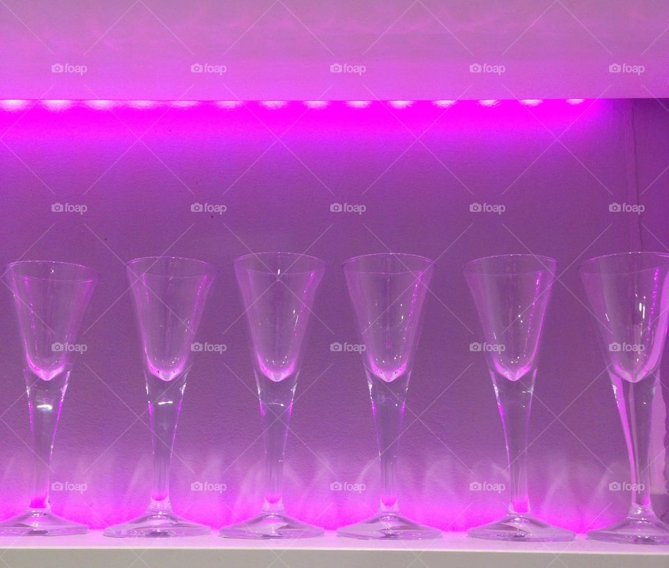 Line of champagne flutes on a shelf with purple ambient lighting 
