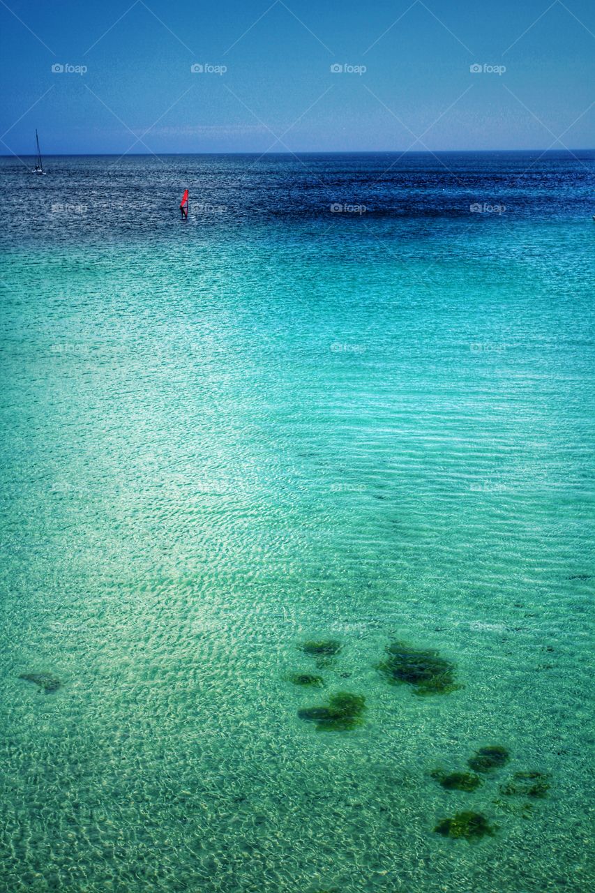 Emerald green sea with a single windsurfer on a hot summer day.