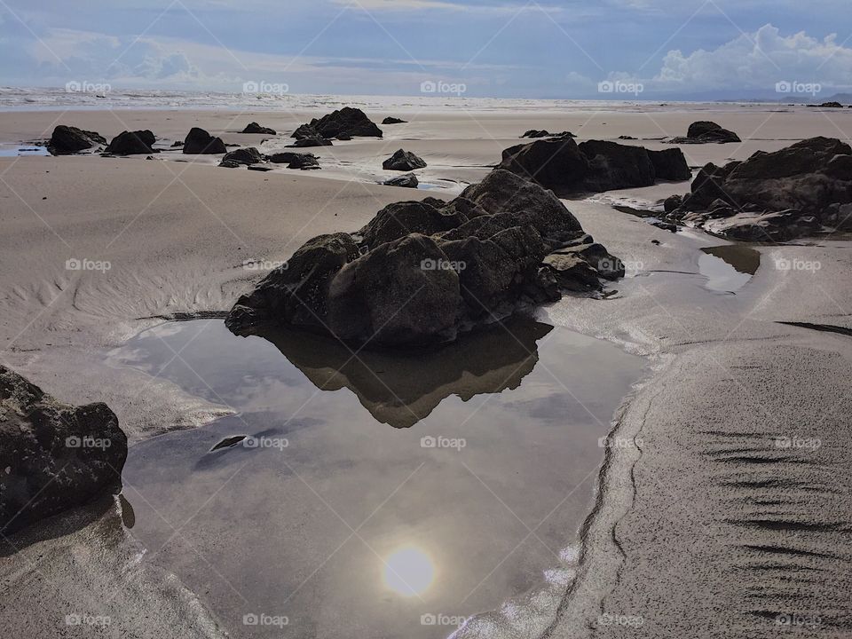 Sun mirroring in the pothole on rocky beach