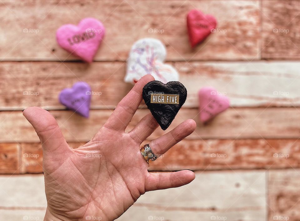 Woman’s hand holding homemade heart Valentines, making salt dough decorations for Valentine’s Day gifts, hand holding high five heart, high five words, high five hand, crafty hearts at home, close up focus on the hearts, making gifts, woman’s hand