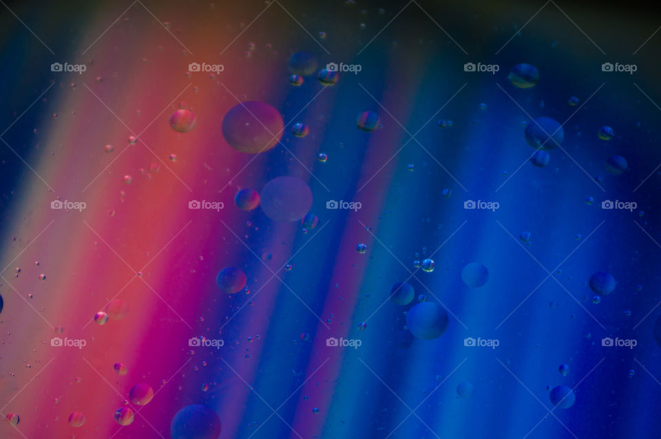 Bubbles of vegetable oil in clear water on a glass and transparent lid from a frying pan on colored paper.