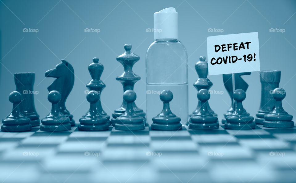 Coronavirus concept image chess pieces and hand sanitizer on chessboard illustrating global struggle against novel covid-19 outbreak with defeat covid-19 sign.