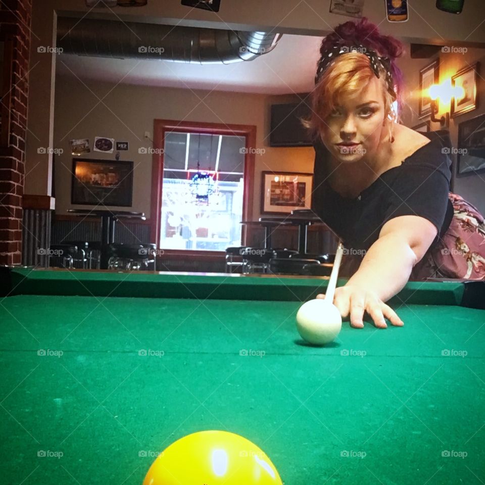 A sly looking woman taking a shot at a game of pool.