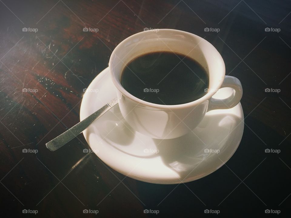 A white cup of espresso coffee on a wooden table. 