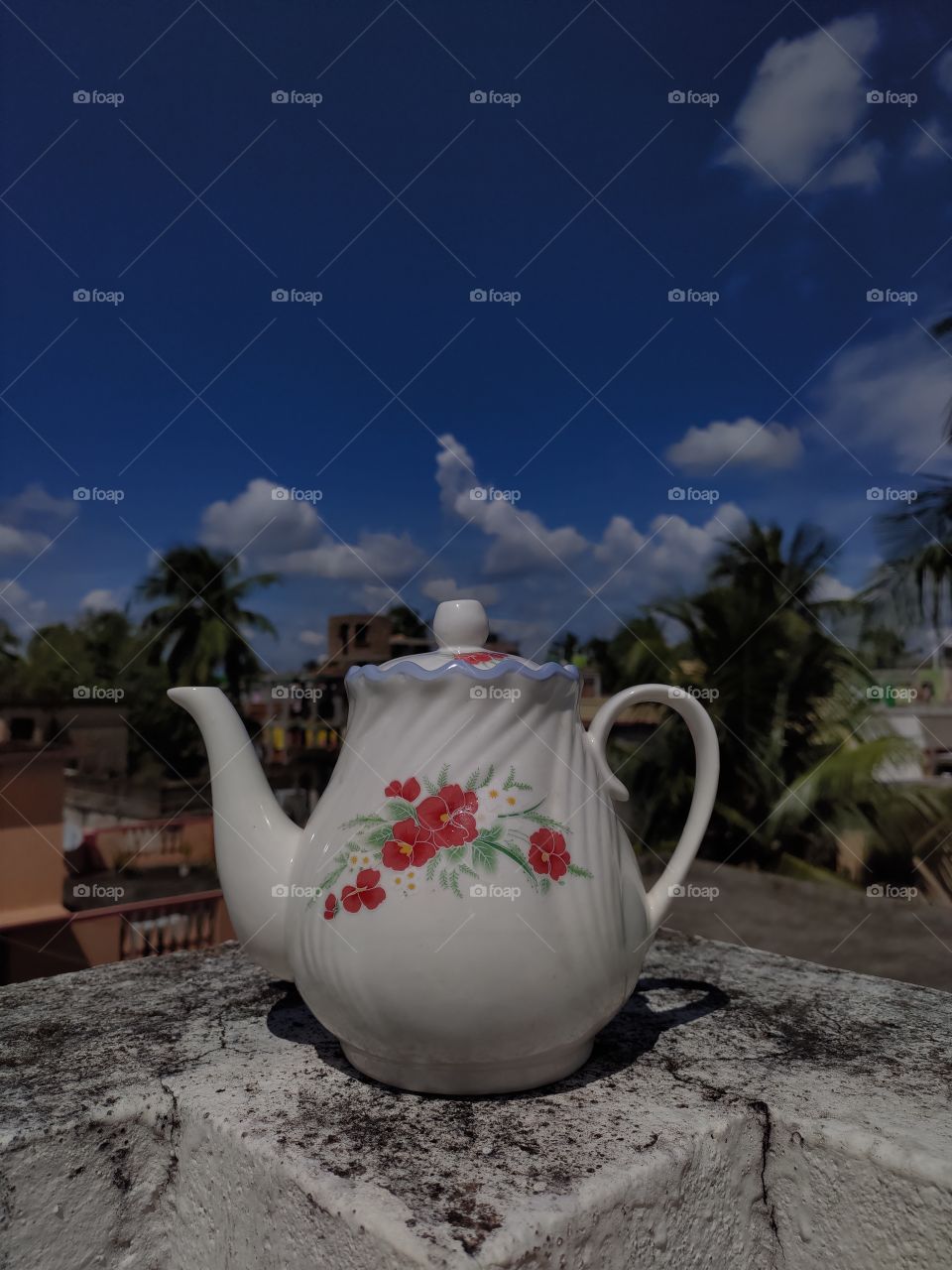 Raw photo of a tea kettle with a bright blue sky with clouds as a background.