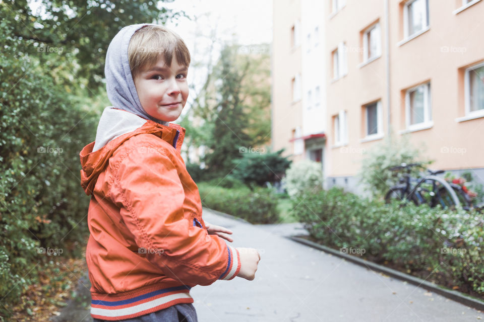 Portrait of boy, outdoors city. Child looking happy, urban background in rainy autumn weather