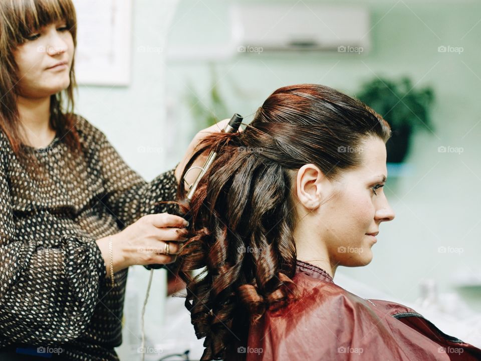 Female hairdresser works on woman hair in salon
