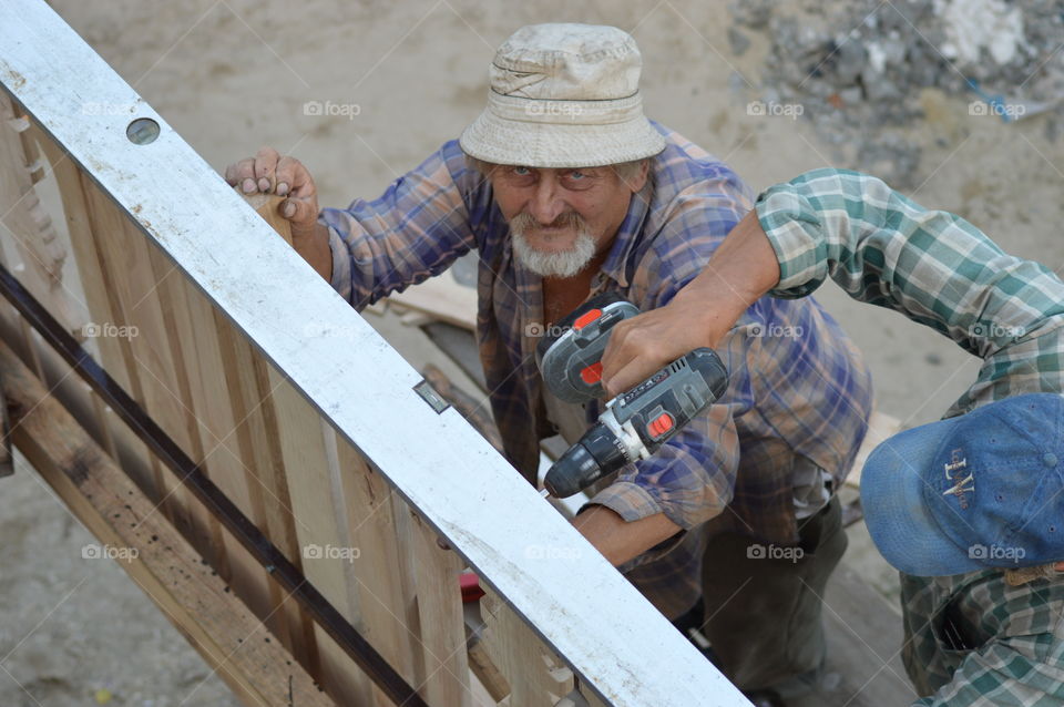 Man's arms drilling wood and a mature labor