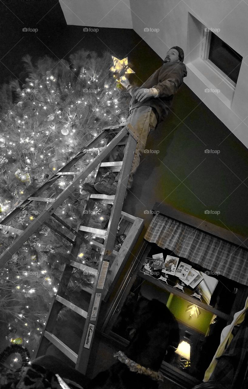 Man standing on ladder decorating christmas tree