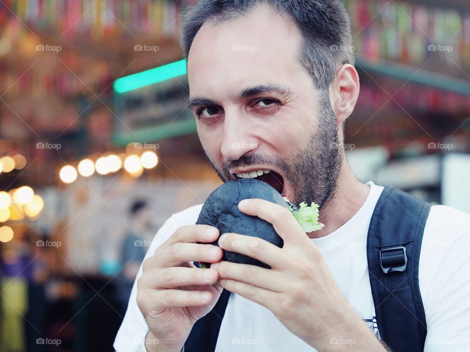 Bearded man eating black burger 