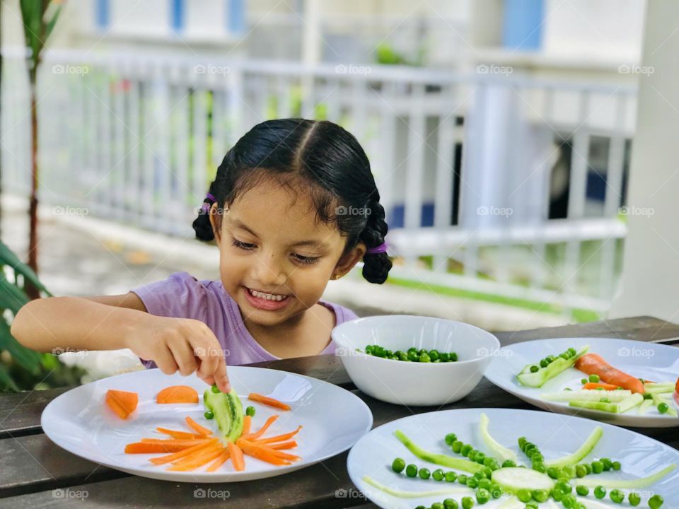 Four years old girl making craft  coconut tree and sun with vegetables like carrots and Greenpeace.