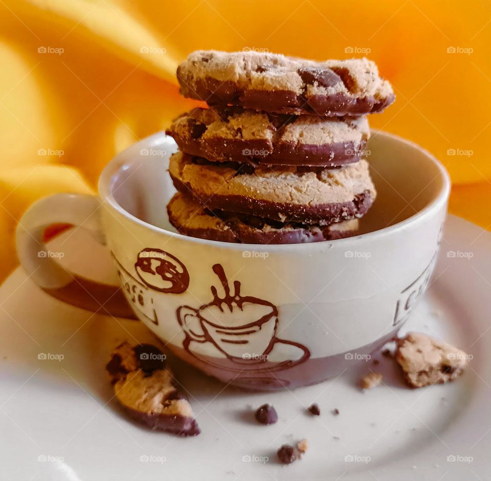 chocolate cookies inside a cup of coffee on a yellow tablecloth background, on a white plate