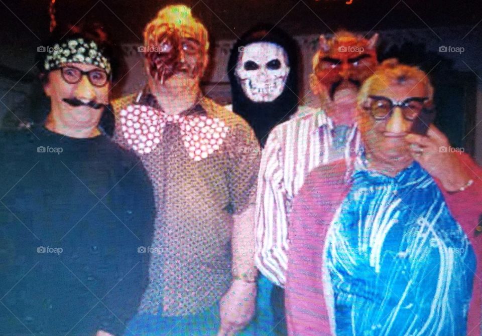 Costumes on family for Halloween portrait. All people wearing masks, standing together in group for picture.