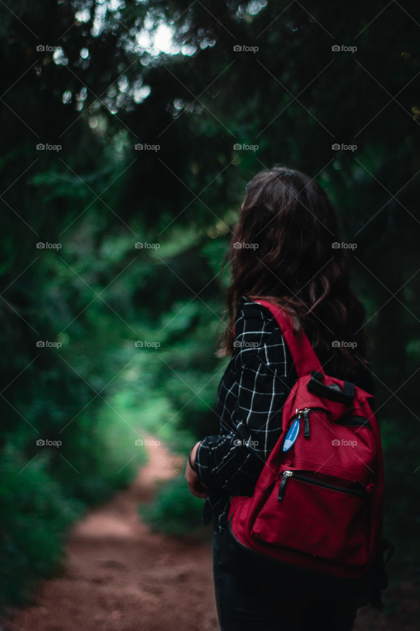 Girl with a red backpack in the forest walking on a lonely path.