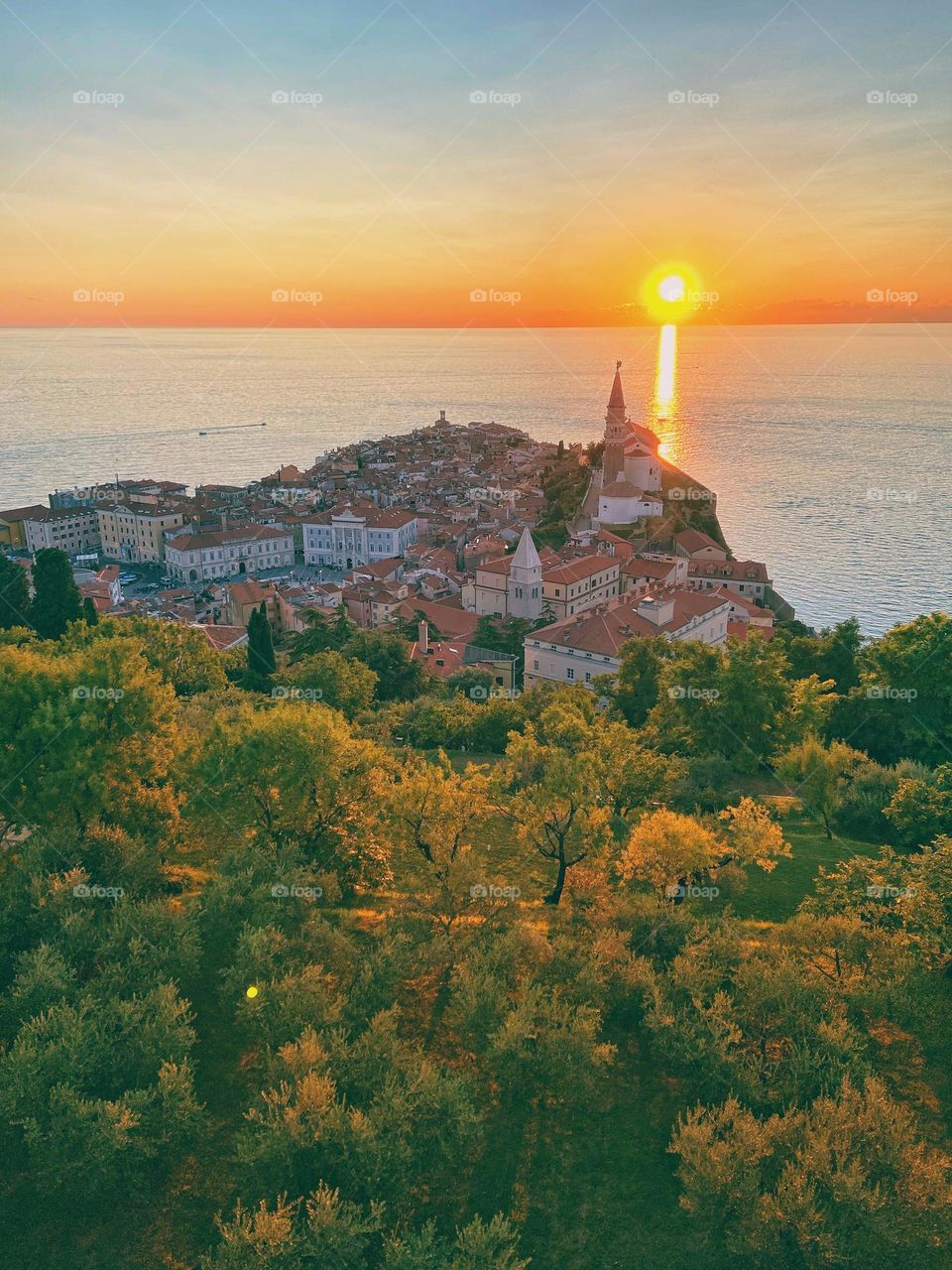 Summer vacation at Piran, Slovenia. Adriatic sea and main church against orange sunset sky. 