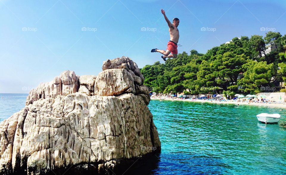 A man jumping off of a rock into clear waters