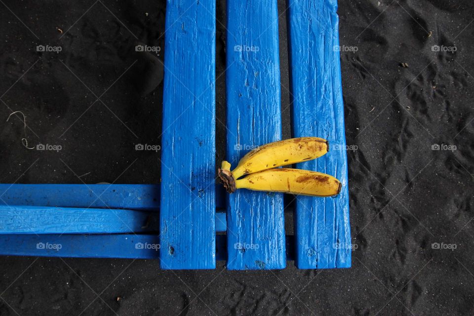 Two bananas lying on a blue table at black sand 