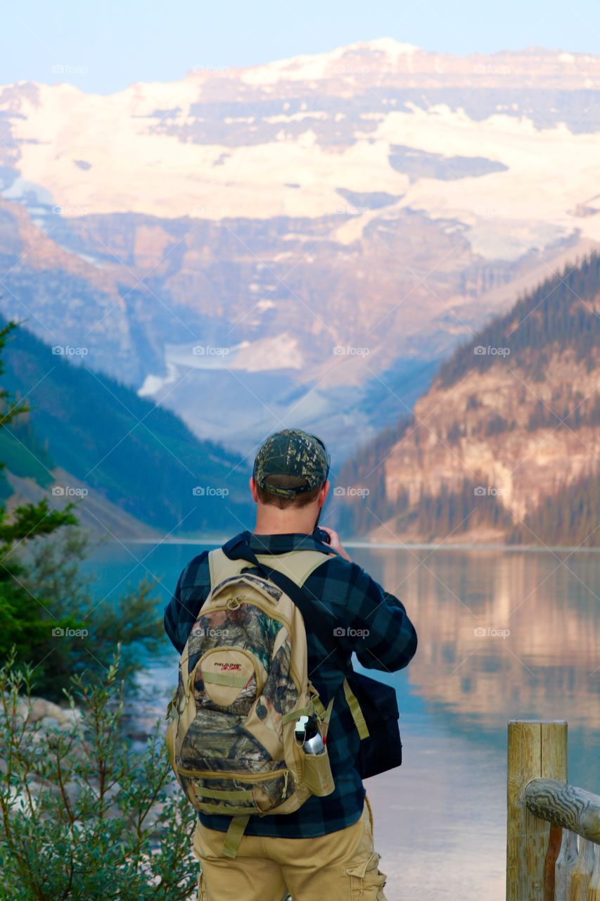 Man in hat and backpack taking photo of beautiful scenic Lake Louise near Banff Alberta in Canada's Rocky Mountains