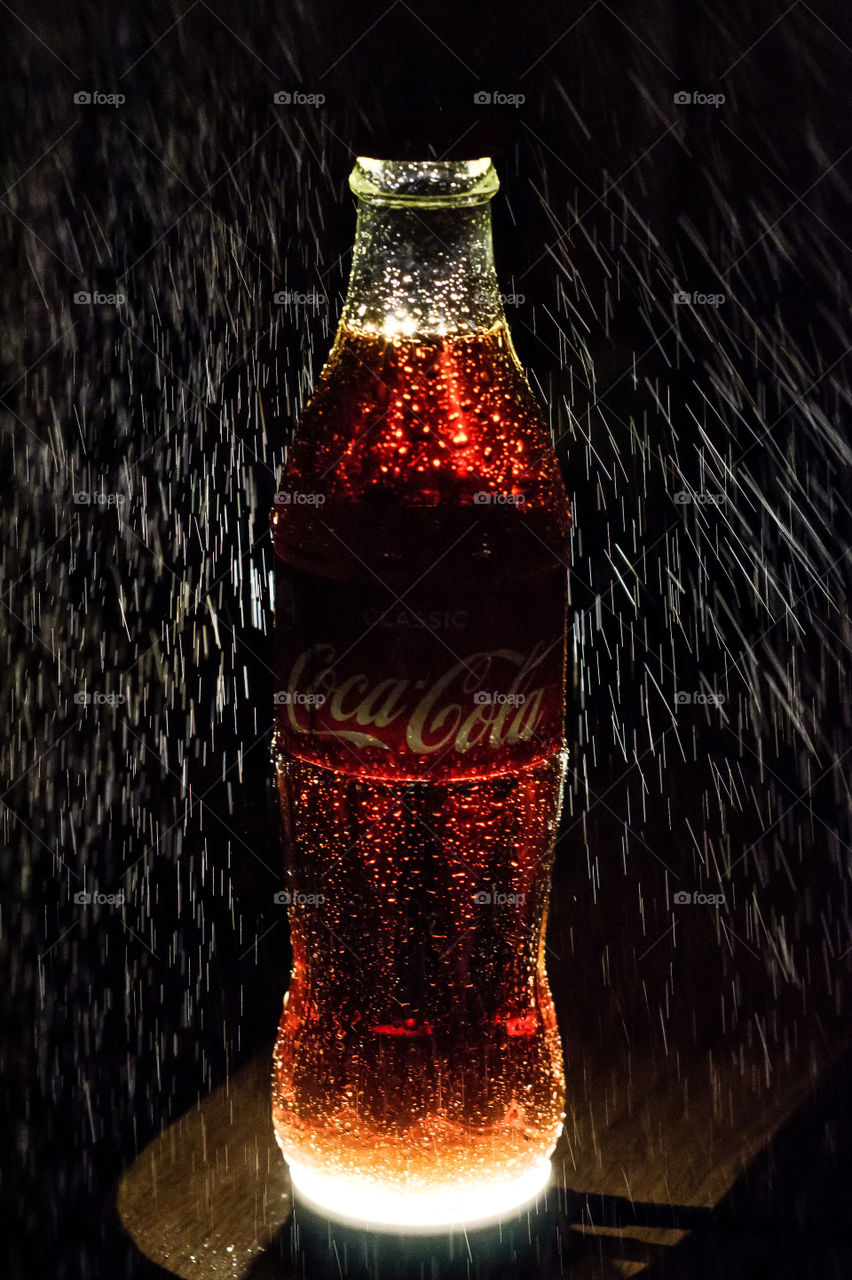 Bottle of Coca-Cola on a black background with water drops.