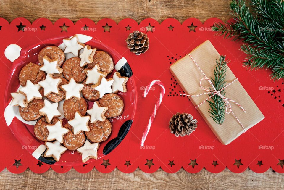 Top view of delicious Christmas cookies on a plate next to gifts and decorations