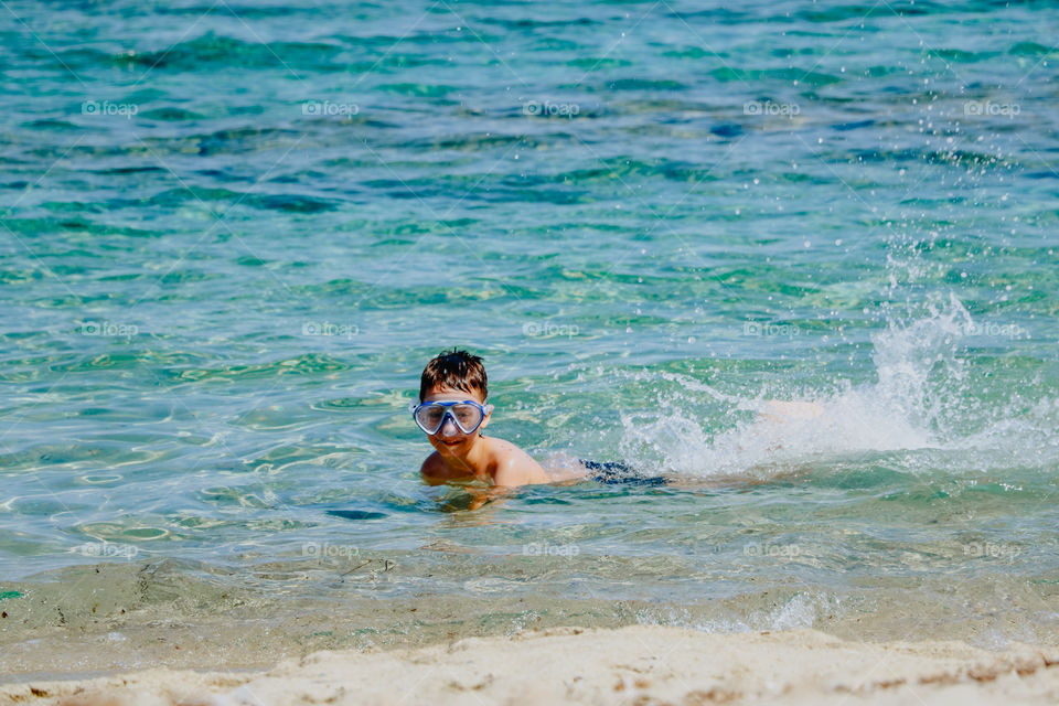 Child with mask swimming in the sea near the shore.