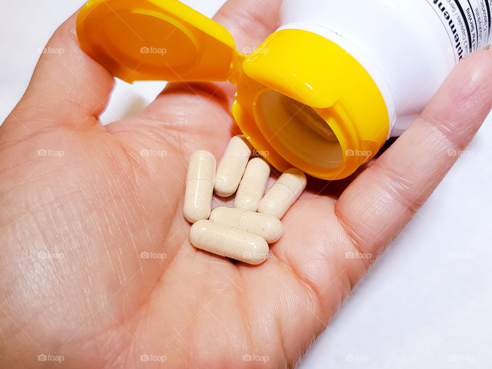 Supplement bottle with yellow cap and six supplement capsules poured in hand with a white background.