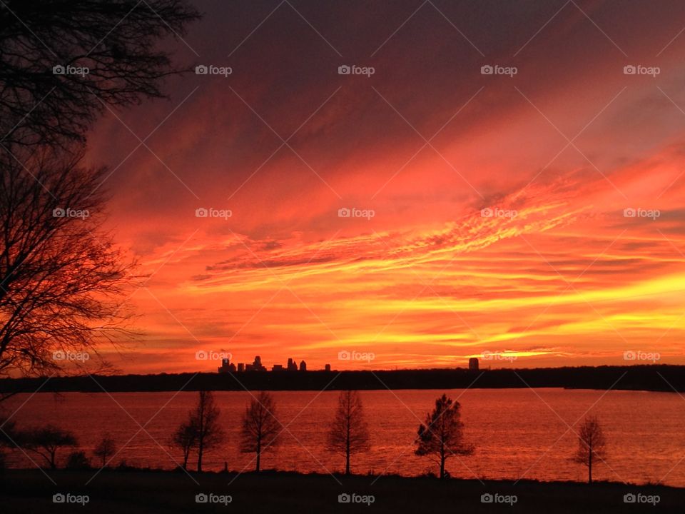 Fiery sunset with view of the Dallas skyline from White Rock Lake with trees in silhouette 
