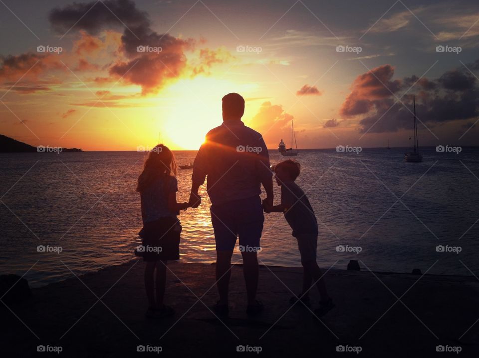 A dad with his son and daughter at sunset in Sint Maarten. Figures are facing the sunset and silhouetted 