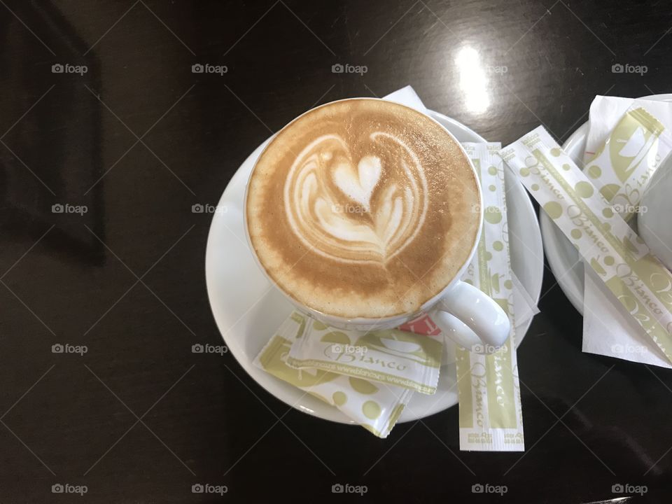 Lovely porcelain cup of coffee with ness coffee in it with small white heart, in the beautiful morning, surrounded by little bags of shugar on a plate.