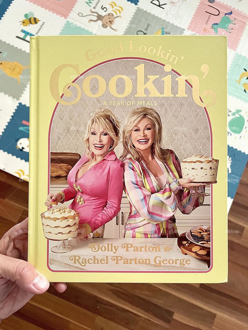 Woman’s hand holds Good Lookin’ Cookin’ Cookbook, Dolly Parton’s Cookbook, ordering Dolly Parton’s new cookbook off of Amazon, Good Lookin’ Cookin’ Cookbook 