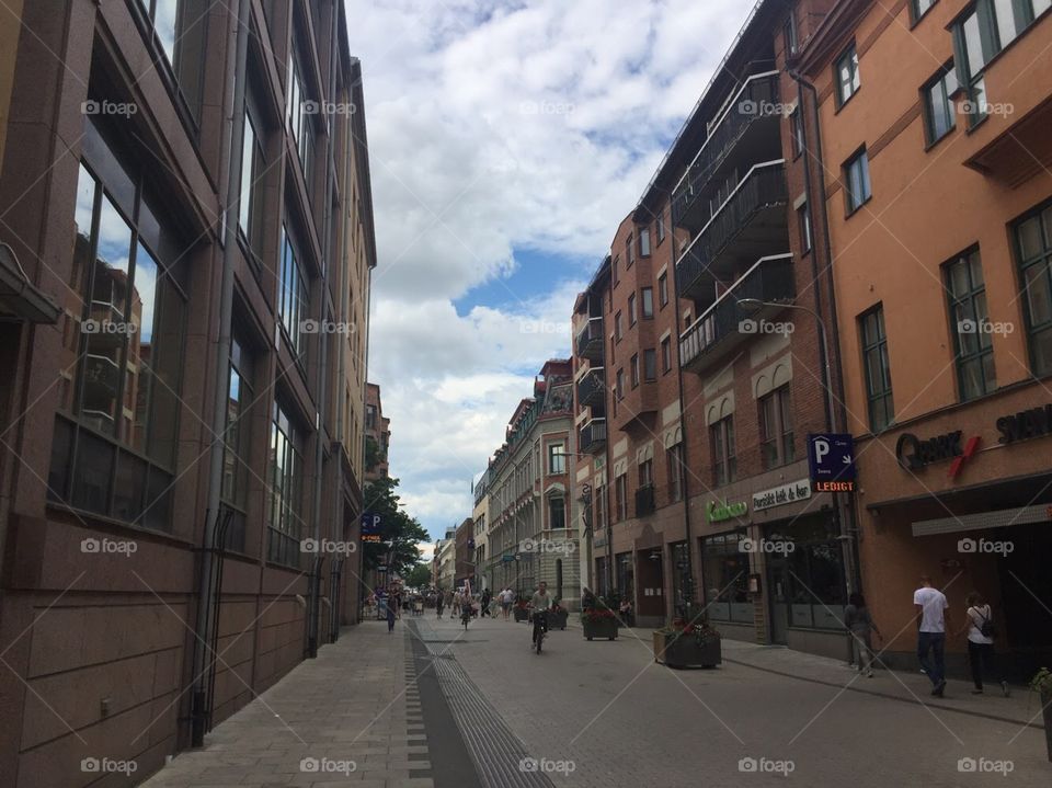 A street in Uppsala, large buildings with many windows painted colorfully. The sky is blue and reflects off of the windows. 