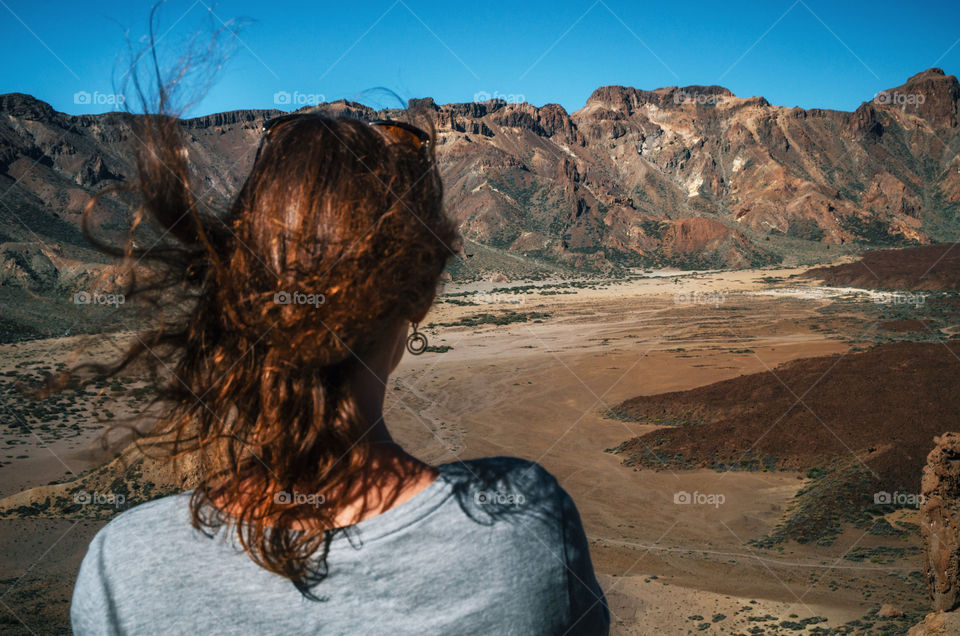 Young woman stands back to the camera and looks at the valley of National Teide Park, Tenerife, Canary Islands, Spain