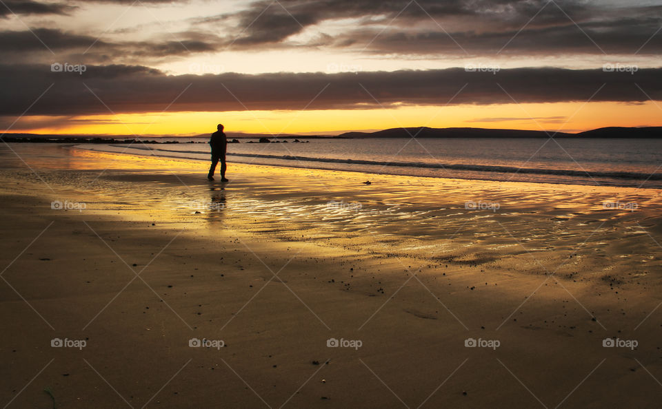 Silhouetteed black man walking down the beach at sunrise