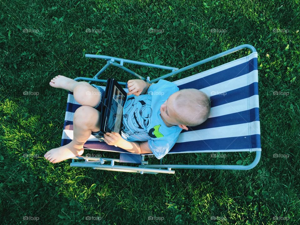 Boy using a tablet sitting in a chair outdoors