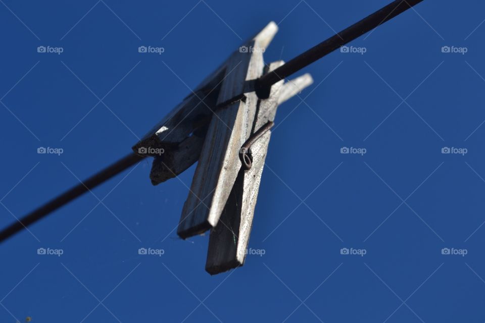 A vivid crisp shot of two old wooden clothespins clothes pegs on a clothesline washlonw against a vivid blue sky