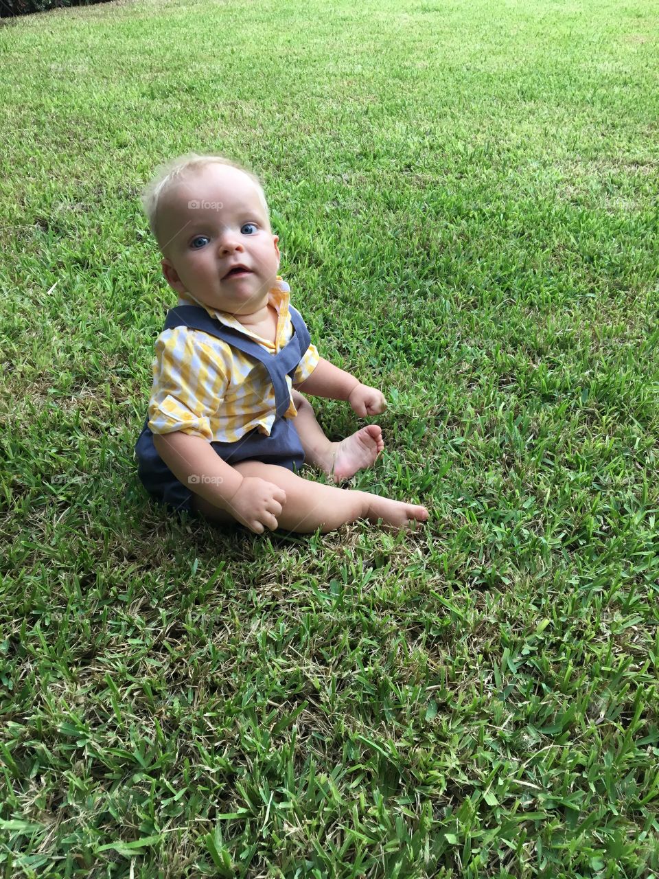 A cute little 6 month old boy playing on the grass 