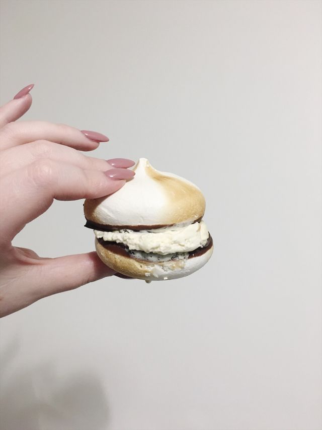 Close up of a hand with pink nails holding a gold meringue against a blank white background