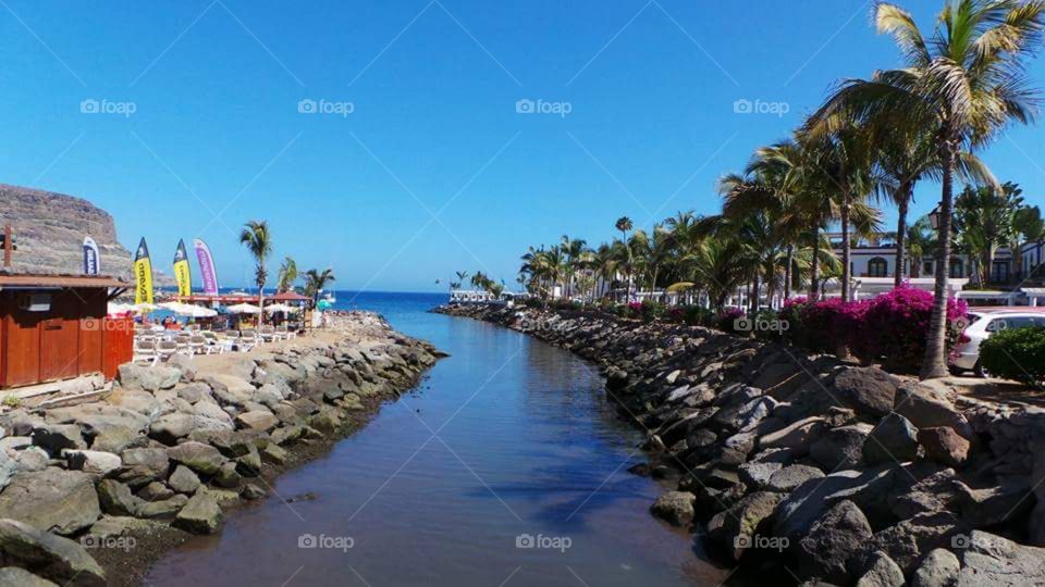 Puerto de Morgan
Gran Canaria
Puerto de Mogán is a picturesque resort and fishing village in the municipality of Mogán, set at the mouth of a steep-sided valley on the southwest coast of the island of Gran Canaria. It attracts many tourists either to stay or on day-visits. Canals linking the marina to the fishing harbour have led to it being nicknamed "Little Venice" or the "Venice of the Canaries". Restaurants and bars fringe the marina and the beach front. On Fridays there is a very popular market which brings in tourists from all over the island.
Puerto de Mogán has very few buildings over two stories high, and the government of Gran Canaria restricts new buildings taller than this.
Puerto de Mogán can be reached via a new extension of the motorway GC1 (opened in March 2013) which terminates just to the north, and is also on several bus routes.
The Canal-like channels linking the marina to the fishing harbour have led to it being nicknamed “Little Venice” or the “Venice of the Canaries”.