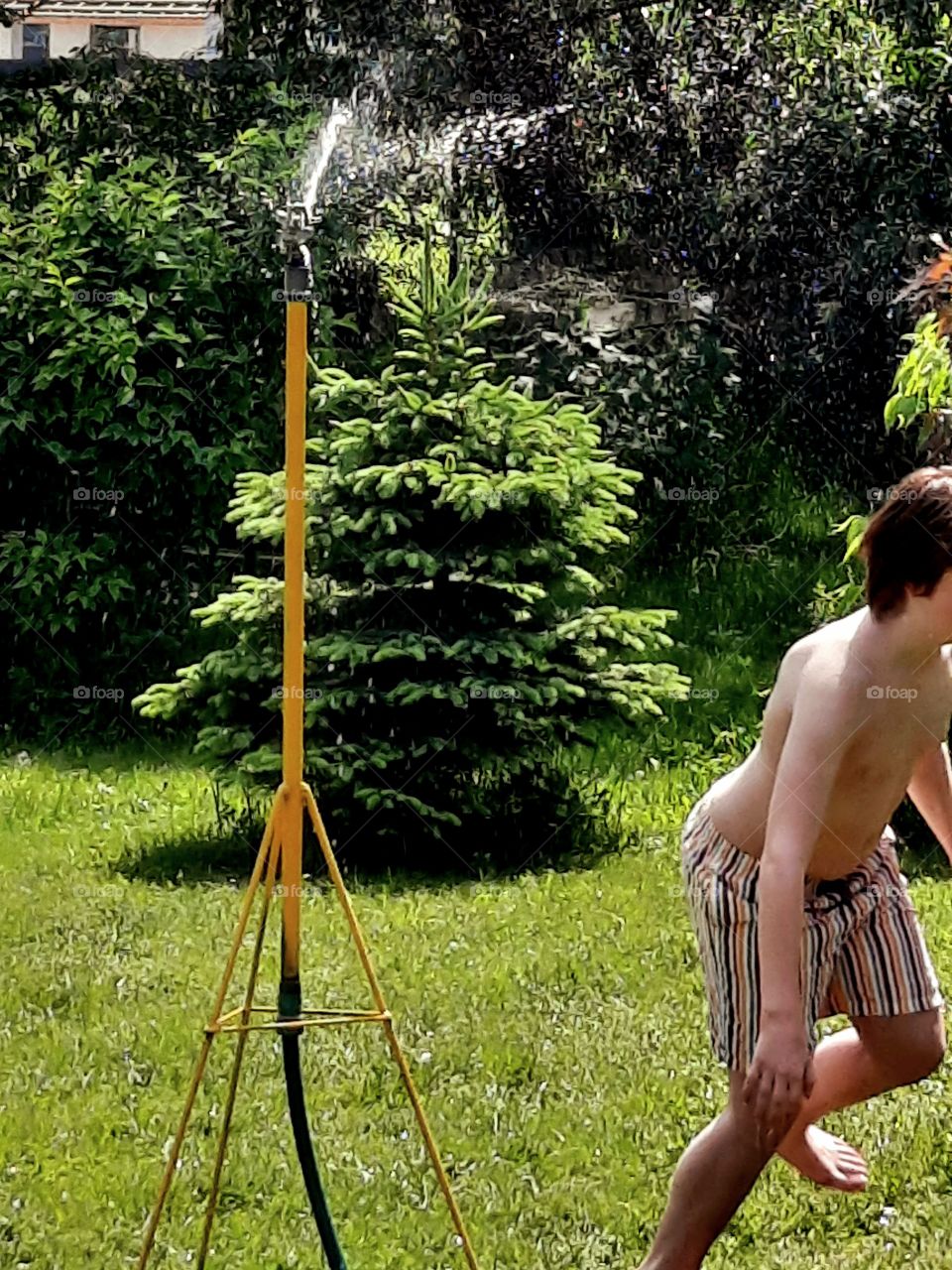 young boy running from water pipe irrigating the garden