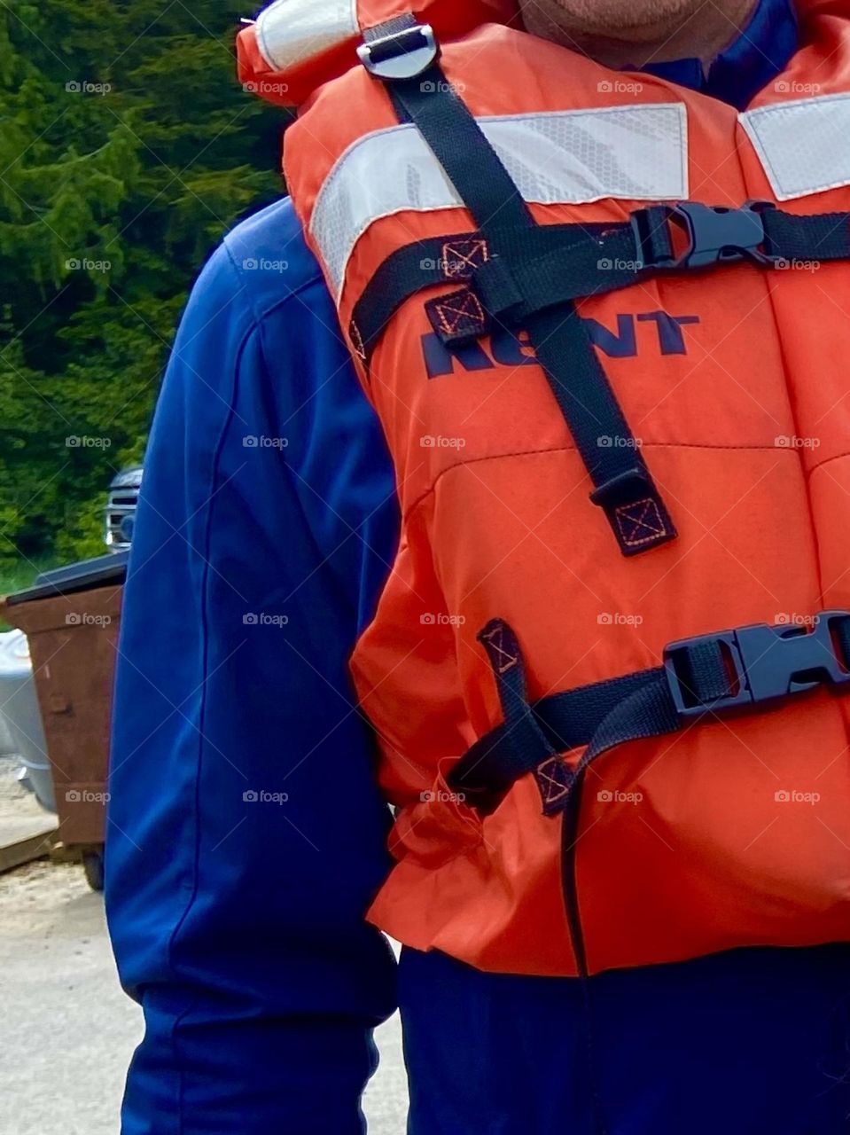 Practicing good water safety with a bright orange life jacket over a blue long sleeved shirt.