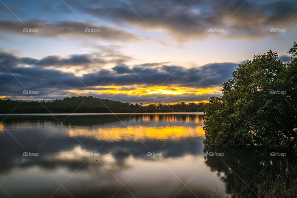 Cloudy sunrise reflected in country river 