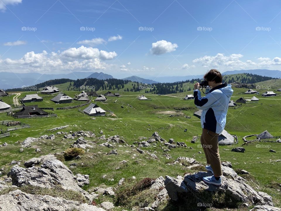 Backstage of the photo shooting in the beautiful Alps mountains in spring in Slovenia.  Young woman photographer doing photos on her phone, camera