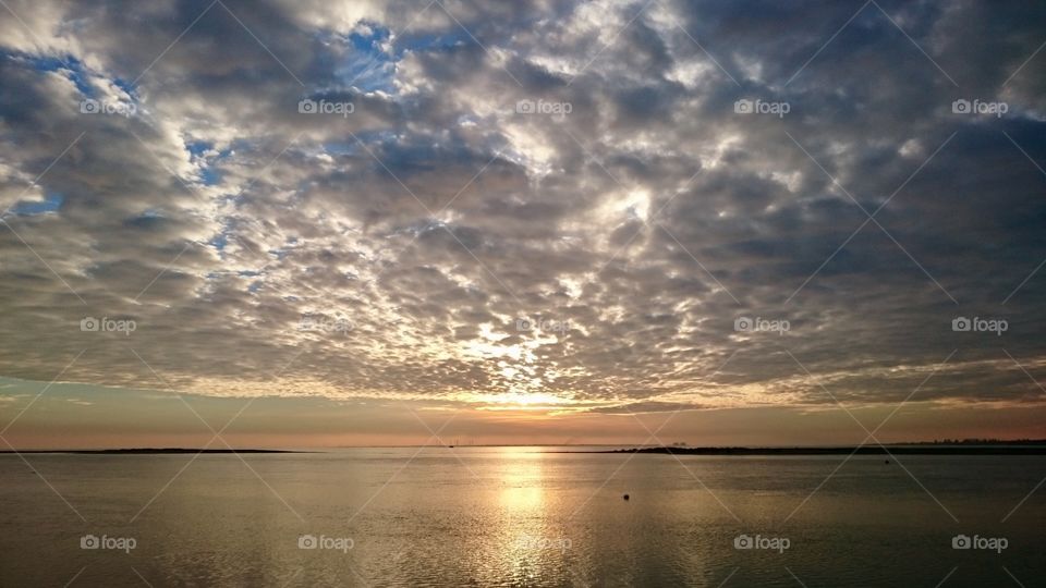 Sun about to set over Point Clear Bay at St Osyth, near Clacton, Essex, against a cloudy sky
