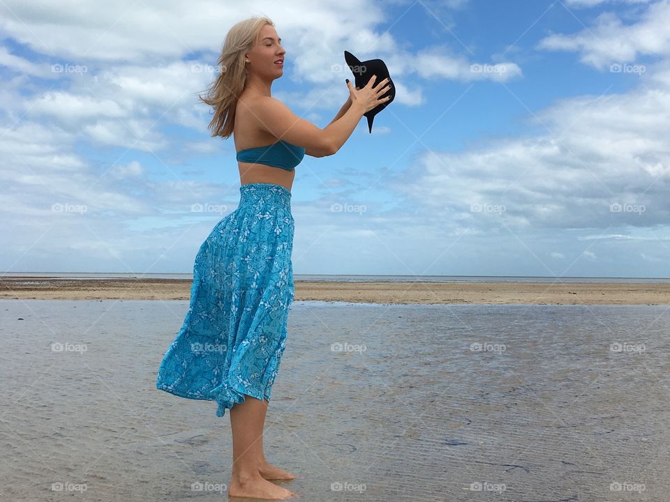 Woman standing on sandy beach with black hat