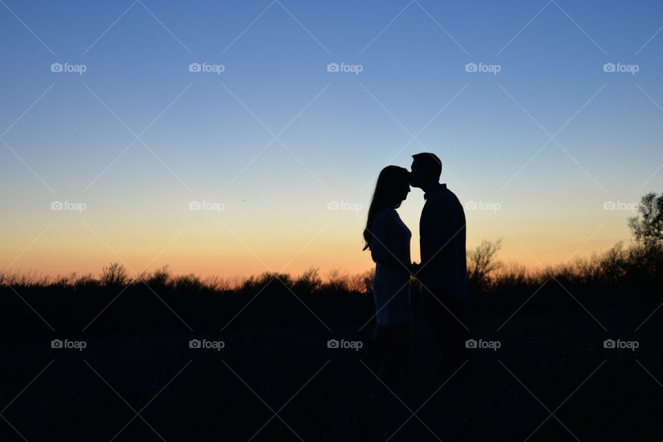 Silhouette of a man kissing woman's forehead