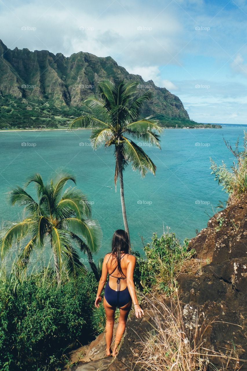 Girl overlooks island and ocean during day hike in Hawaii.