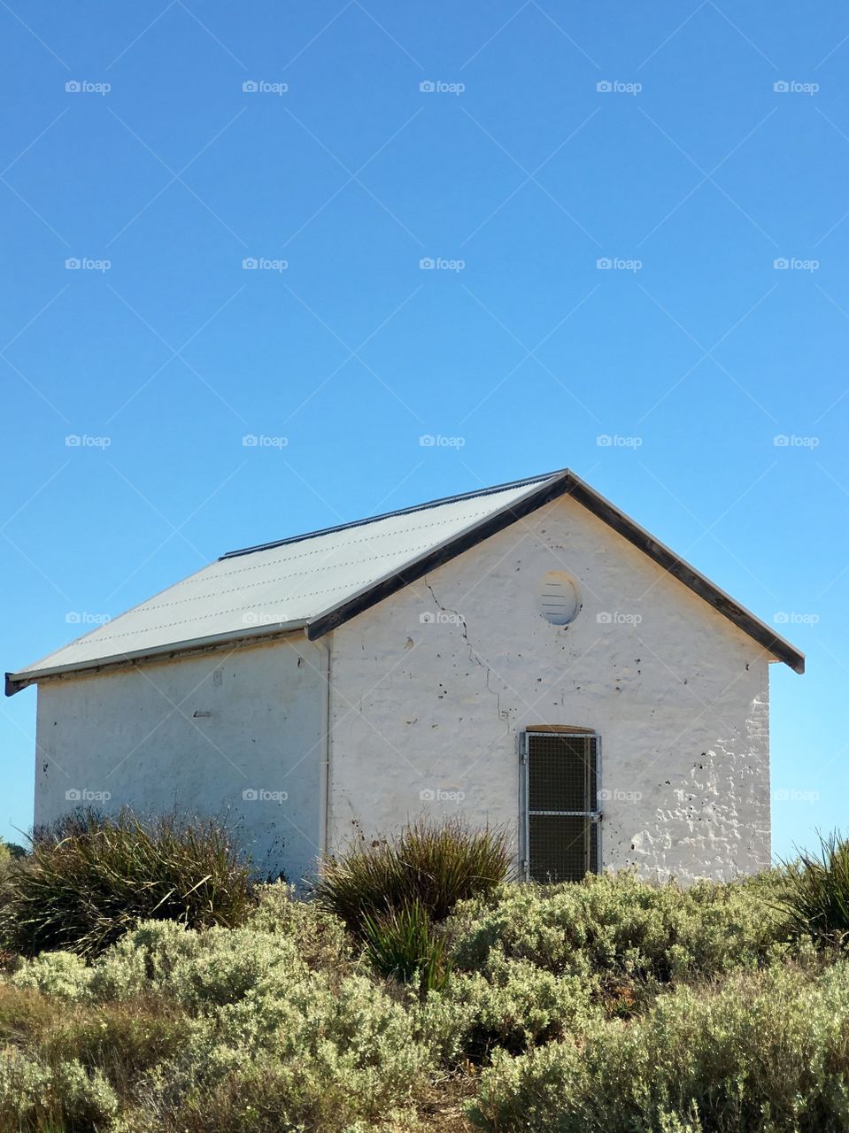 White stone heritage lighthouse keepers house, agains ocean horizon on vivid blue day, picturesque, 