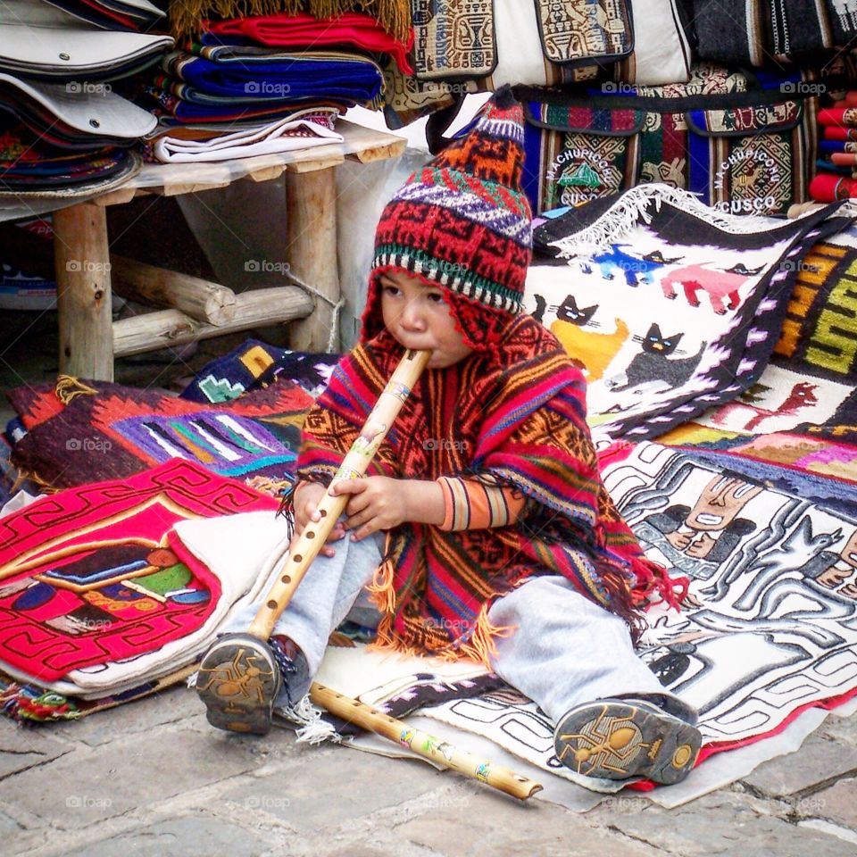Cute little boy playing flute while his mommy sells souvenirs to tourists