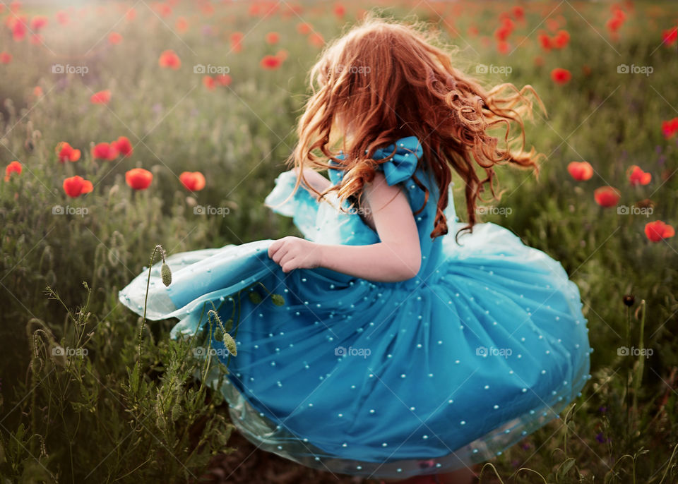 Little redhair girl spinning in a beautiful blue dress in a poppy field